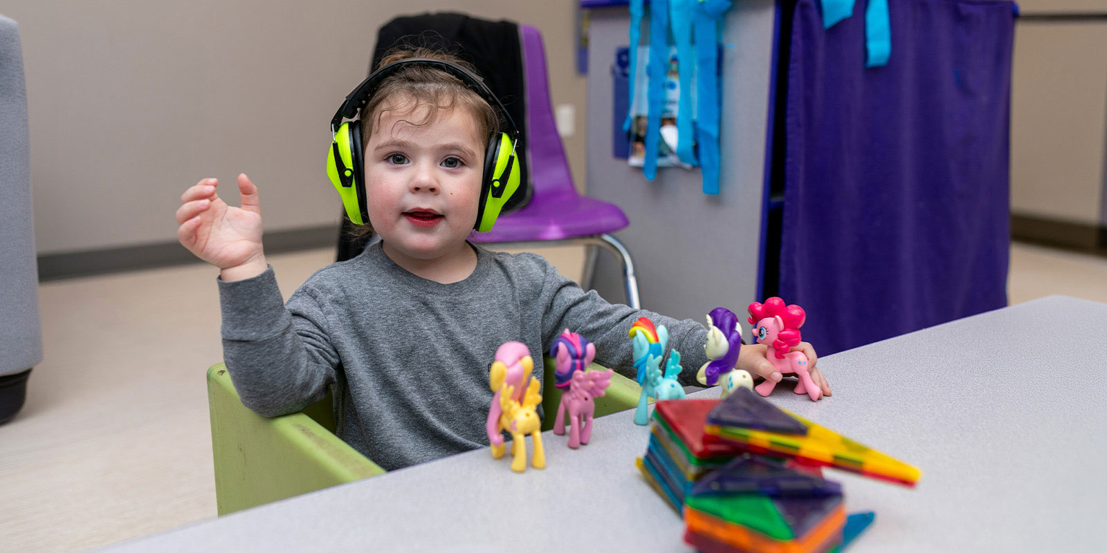 child wearing noise cancelling headphones and playing with my little pony toys at a table