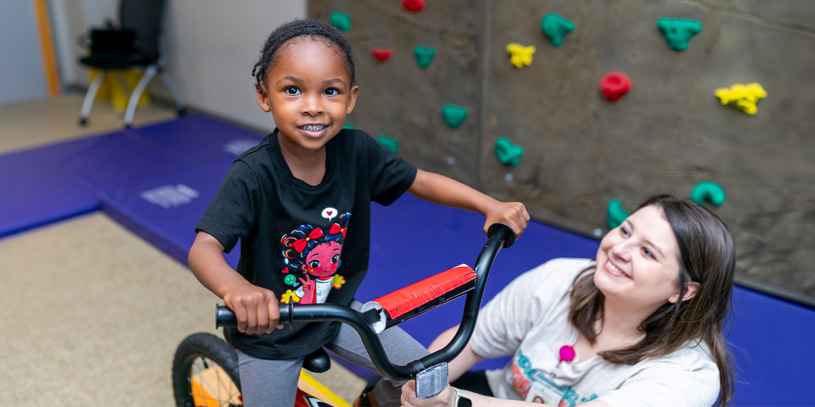 child receiving help learning to ride back in a playroom setting