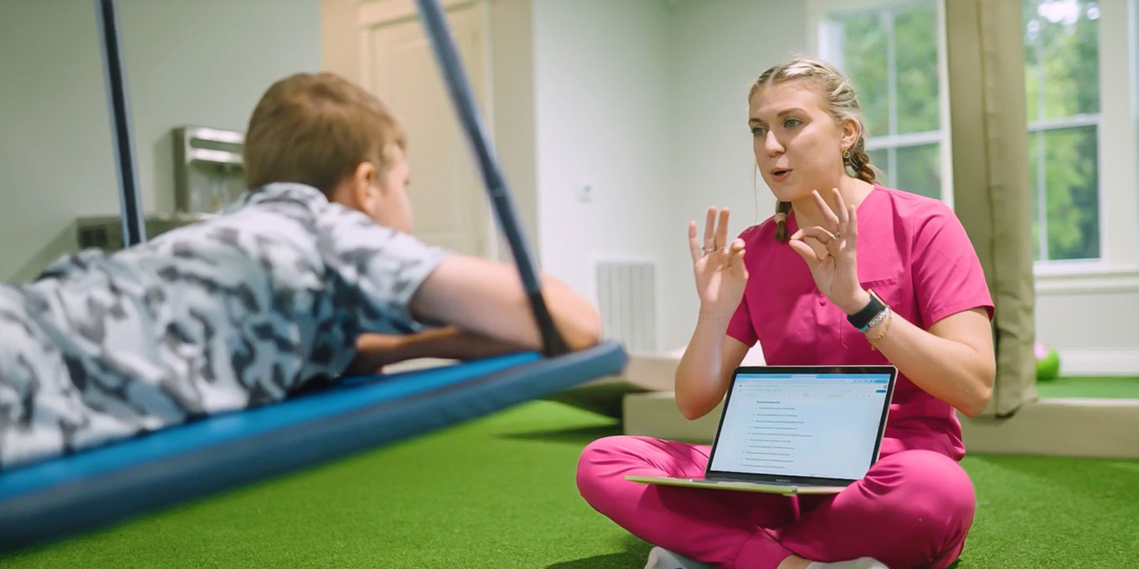 child on swing in playroom working with speech therapist sitting on floor